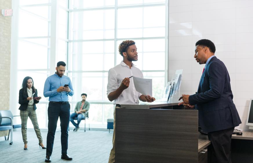 man at a counter asking for help while others are waiting in line