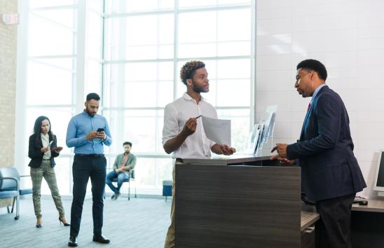 man at a counter asking for help while others are waiting in line