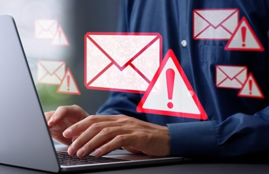 hands typing on laptop with envelopes and warning signs floating by