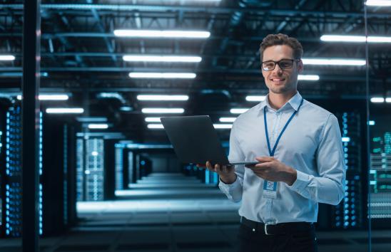 Successful Data Center IT Specialist Using Laptop Computer. Server Farm Cloud Computing Facility with System Administrator Working. Data Protection Engineering Network for Cyber Security.